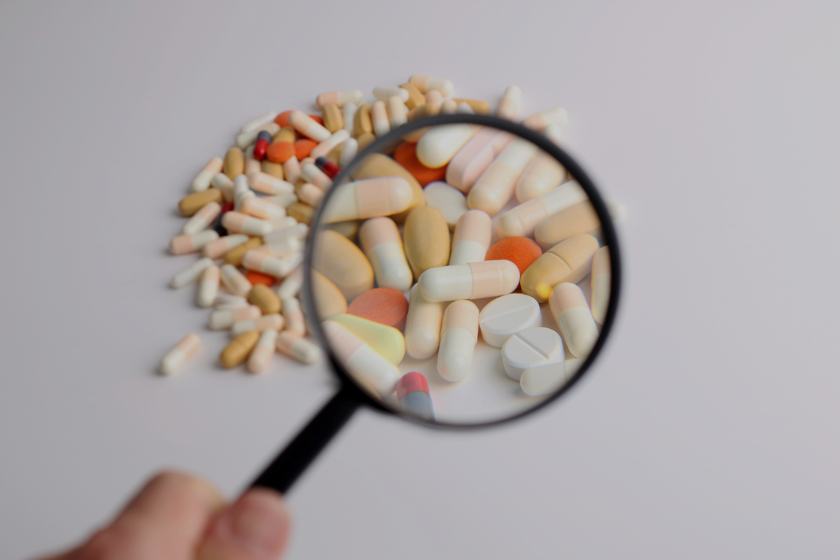Magnifying glass over supplement capsules depicting FDA review of NMN quality and safety.