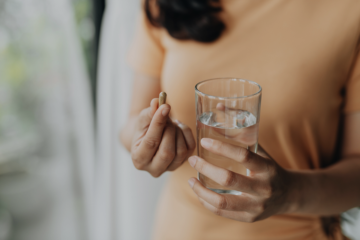 Woman holding glass of water and capsules symbolizing oral NAD+ supplement intake.